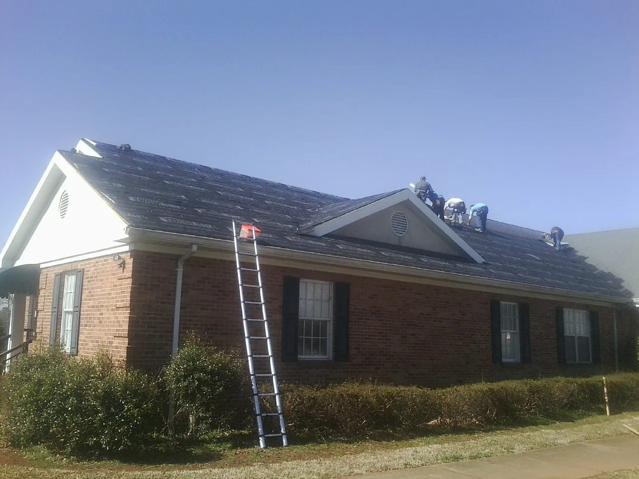Crew tearing shingles off a brick ranch roof with a ladder set — Emergency Roof Repair work by our crew in King City