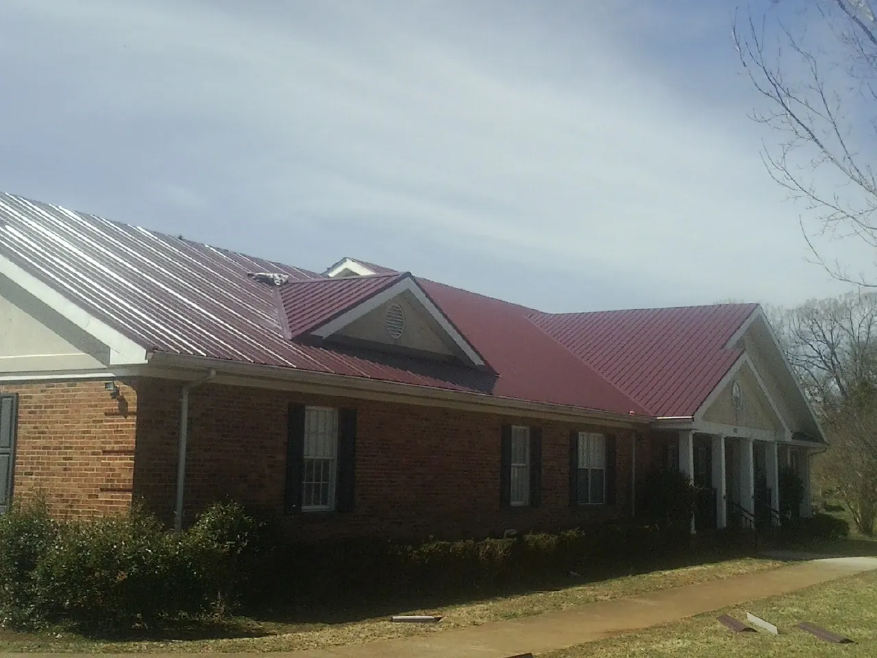 Red metal roof with gabled entries on a long brick building, from a Hail Damage Roof Repair job in King City