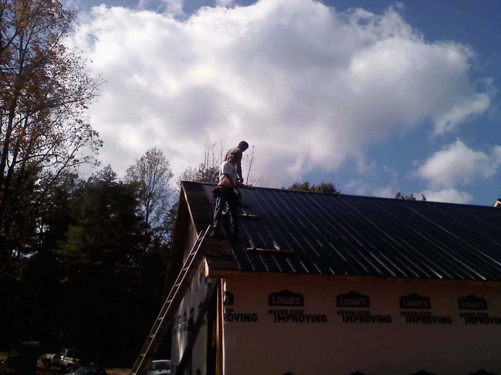 Roofer fastening dark metal panels high against a cloudy sky, from a Roof Inspection job in King City