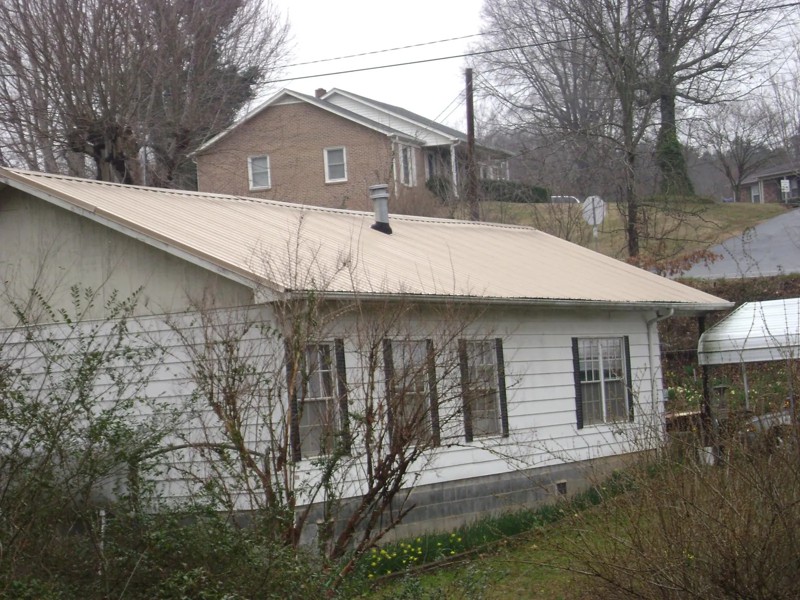 Tan metal roof on a white sided house set into a hillside — Commercial Roofing by Roofing Brothers in King City